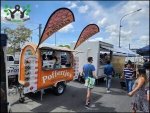 A man with a green bag is walking past a food truck that sells pancakes.