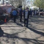 A man with a white beard and hat walks down a street, surrounded by people and tents.
