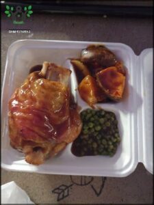 A meal in a white container with a piece of meat, potatoes, and peas.