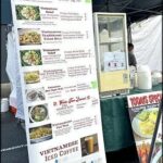 A menu board for Vietnamese food is displayed at a food stand.