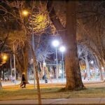 A park at night with a lighted playground and a person walking by.