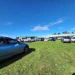A parking lot filled with cars and trucks, with a blue car parked in the foreground.