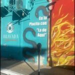 A parking meter is located in front of a colorful wall with a snake painted on it.
