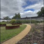 A pathway in a garden leads to a fence, with a metal fence and a metal walkway.