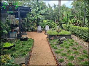 A pathway leads to a patio with two chairs and a bench.