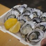 A person holds a container of oysters and a lemon wedge.