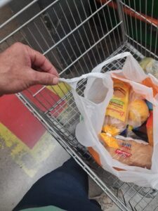A person is holding a bag of bread in a grocery cart.