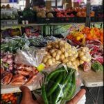 A person is holding a bag of green beans at a market.
