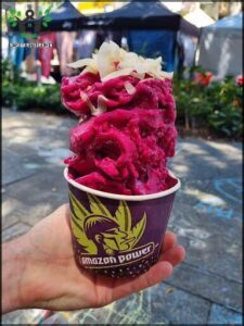 A person is holding a cup of purple food, possibly a frozen treat, in front of a crowd of people.