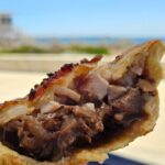 A person is holding a half-eaten pastry with meat and cheese.