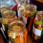 A person is holding a jar of food, which contains carrots and cauliflower.