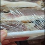 A person is holding a piece of meat wrapped in plastic.