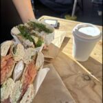A person is holding a sandwich and a cup of coffee.