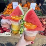 A person is holding two cups of fruit, one containing watermelon and the other containing orange slices.