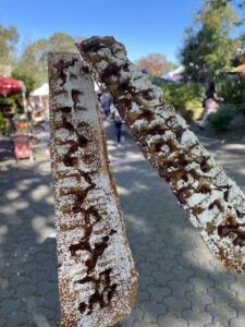 A person is holding two donuts with chocolate drizzled on them.