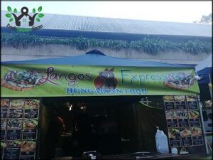 A person is standing in front of a food stand, which is advertising Hungarian food.
