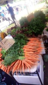 A pile of carrots and other vegetables are displayed at a market.