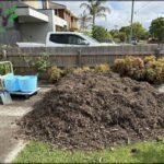 A pile of wood chips sits on a sidewalk, ready to be used for mulching or other purposes.
