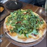 A pizza with greens and olives on top.