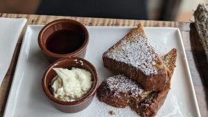 A plate of food with a bowl of sauce and a sandwich with powdered sugar on top.