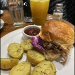 A plate of food with a sandwich, potatoes, and a glass of orange juice.