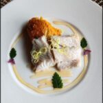 A plate of food with a slice of fish and a side of orange sauce.
