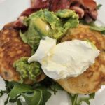 A plate of food with a variety of items, including a sandwich, a pile of bacon, and a side of avocado.