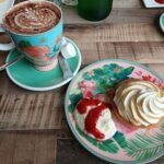 A plate of food with a white and pink floral plate, a cup of coffee, and a pastry.
