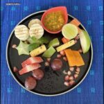 A plate of fruit and vegetables, including bananas, apples, and carrots, is displayed on a table.