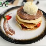 A plate of pancakes with chocolate sauce and strawberries on top.