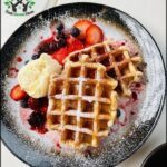 A plate of waffles with strawberries and blueberries on top.