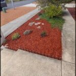 A red mulch bed with a tree in the corner.