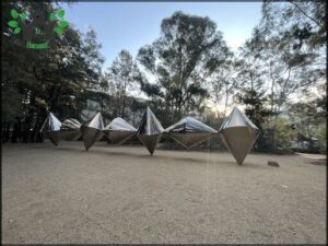 A row of silver sculptures are lined up in a field.