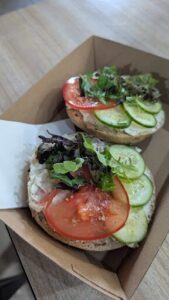 A sandwich with tomatoes, lettuce, and cucumbers is served in a cardboard box.