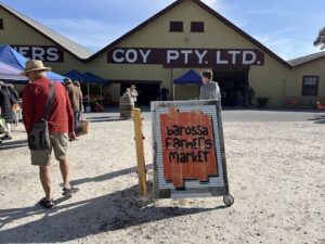 A sign advertising a farmers market is displayed in front of a barn.