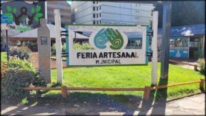 A sign in a park with a green and white design that says "Feria Artesanal".