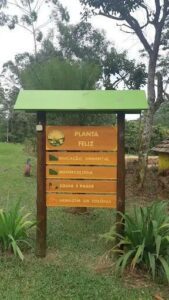 A sign that says "Planta e feliz" is displayed in front of a forest.