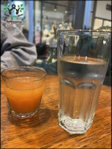 A small glass of orange juice sits next to a larger glass of water on a table.