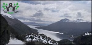 A snowy mountain overlooks a lake and a valley.