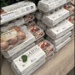 A stack of organic eggs and a bag of organic meat sit on a table.