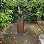 A statue of a bird is sitting on a pedestal in a garden.