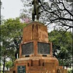 A statue of a man standing on a pedestal is located in a park.