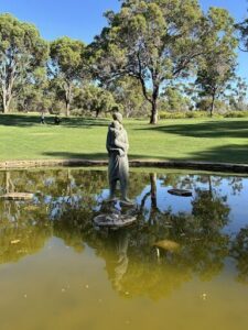 A statue of a person is sitting on a pedestal in a pond.