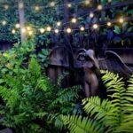 A statue of a woman with angel wings is surrounded by greenery and lights.