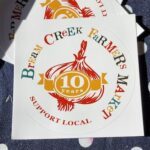 A sticker for the Creek Farmers Market is displayed on a table.