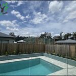 A swimming pool with a fence and a house in the background.