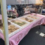 A table filled with various types of cookies and pastries, with a woman standing behind it.