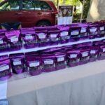A table full of bags of chocolate, with a red car parked in the background.
