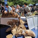 A table full of bread and bags of bread, with people standing around it.