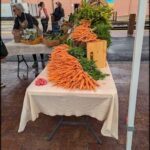 A table full of carrots and other vegetables is set up in a market area.